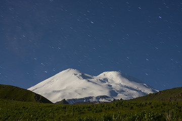 Snowy mountain Elbrus in moonlight and star tracks at night