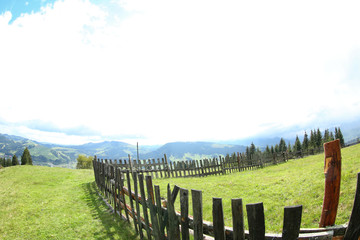 Fototapeta premium Wooden fence on green hills in mountains