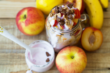 Slices of apple, peach, nectarine, plum and banana blended with yogurt and chocolate corn flakes on wooden table, top view