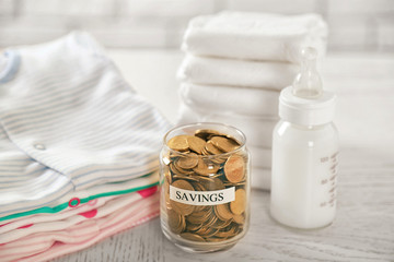 Parenting expenses concept. Glass can with coins, feeding bottle and pile of diapers