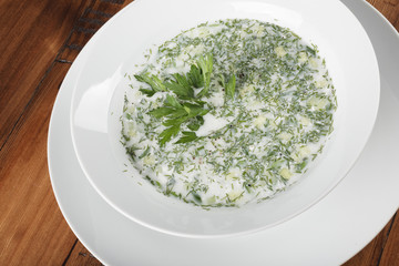 Russian anв ukrainian traditional cold soup (okroshka) in a white plate. Wooden background