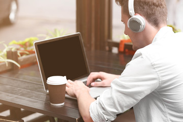 Handsome man with laptop listening music in cafe