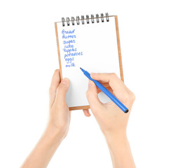 Hands holding pen and notepad with shopping list on white background