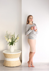 Beautiful woman with cup of coffee on light wall background