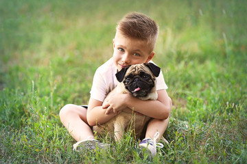 Cute boy with pug dog on green grass