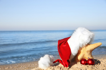 Obraz na płótnie Canvas Santa hat with sea star and toys on beach. Christmas holiday concept