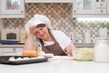 Уставшая женщина повар сидит за столом на кухне 