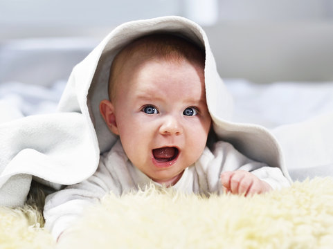 Cute baby hiding under a sheep fur. Beautiful, smiling baby on a white bedding, close-up shot.