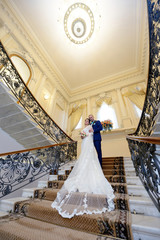 Wedding couple indoors is hugging each other. Beautiful model girl in white dress. Man in suit. Beauty bride with groom. Female and male portrait. Woman with lace veil. Cute lady and handsome guy