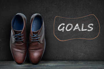 Goals text on black board and business shoes