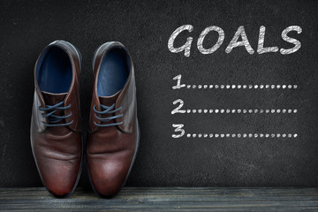 Goals text on black board and business shoes