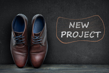 New Project text on black board and business shoes