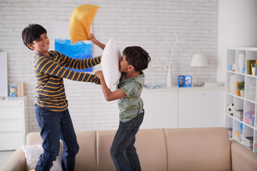 Two brothers fighting with pillows at home