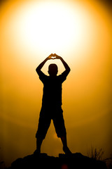 Silhouetted friend forming a heart symbol at golden hour sunset