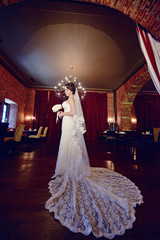 Beauty bride in bridal gown with bouquet and lace veil indoors. Beautiful model girl in a white wedding dress. Female portrait of cute lady. Woman with hairstyle