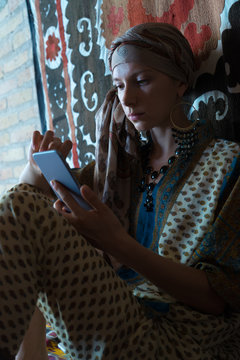 The girl from Central Asia in national costume, spending time with your phone