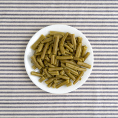 Plate of organic cut green beans on a striped tablecloth.