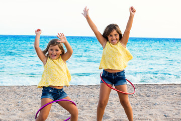 Cute girls dancing with plastic rings on beach.