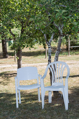 White plastic chairs outside in a garden on green lawn by a pond or lake in the afternoon sun and a peaceful relaxing serene tranquil setting