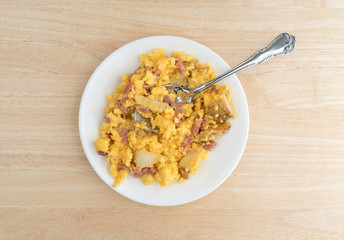 Ham eggs and potatoes breakfast TV dinner on a plate atop a wood table.