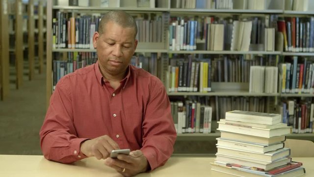 African american man using cellphone in library