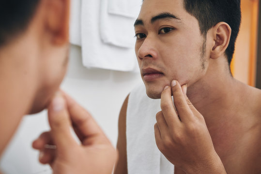 Young man looking at pimple on his chin