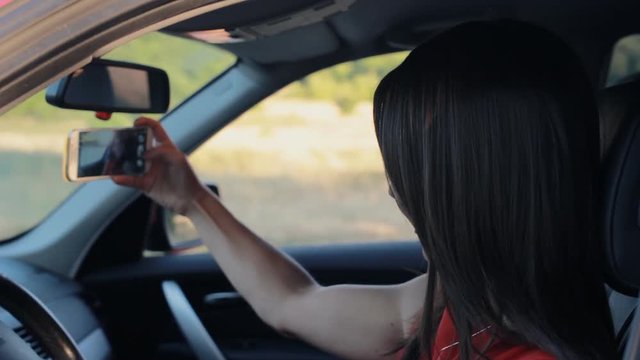 Attractive young woman taking selfie on the phone while sitting in her car
