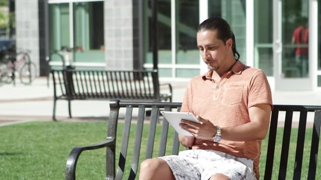Man using tablet sitting on park bench