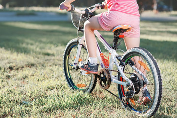 Fototapeta na wymiar Little brunette girl riding bicycle in the park at sunset
