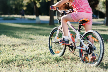 Fototapeta premium Little brunette girl riding bicycle in the park at sunset