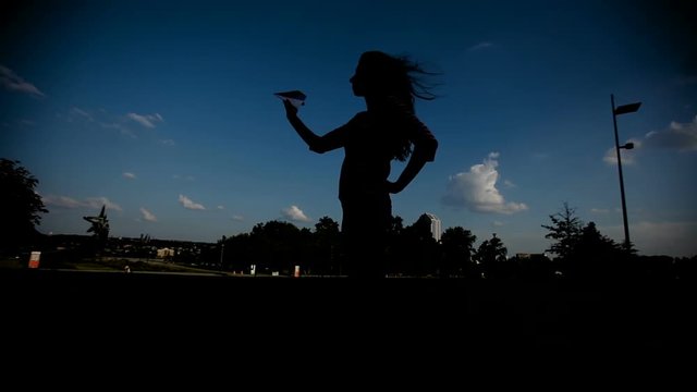 silhouette of a woman holding a paper plane in the hand against the sky