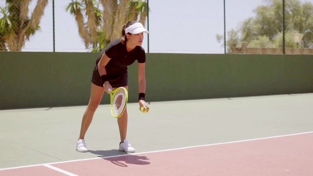 Athletic woman tennis player serving the ball tossing it in the air as she prepares to hit it behind the baseline on a court