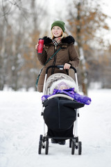 Fototapeta na wymiar Young mother walking with baby in stroller in winter
