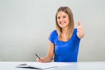 Beautiful female student is studying and showing thumb up.
