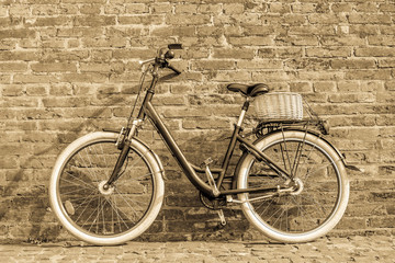 Black retro vintage bicycle with old brick wall and. Retro bicycle with basket in front of the old brick wall. Old photo effect applied. Toned. 