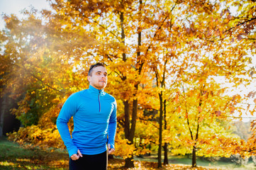 Young handsome athlete running outside in sunny autumn nature