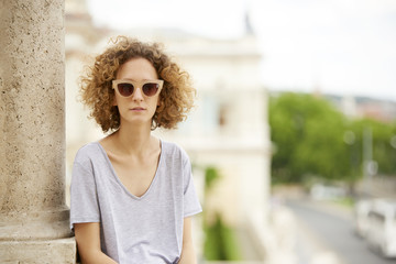 Summer day in the city. Close-up portrait of young confident woman wearing sunglasses and smiling.