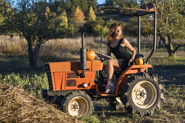 Young female sitting on tractor in rural landsape during fall with pumpkins