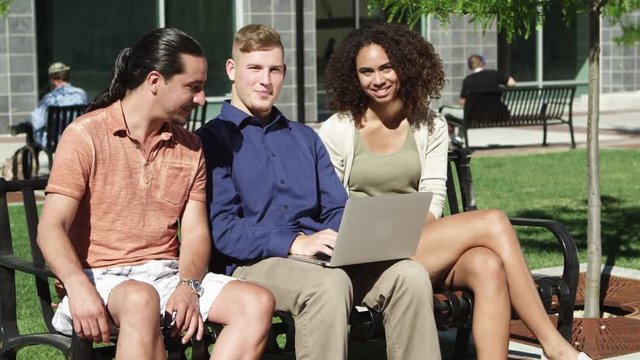 Portrait of friends sitting on park bench with laptop