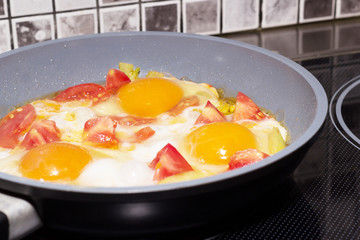 Fried eggs with vegetables in a frying pan on the electrical stove
