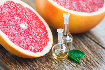 Essential oil in glass bottle with fresh, juicy grapefruit and green leaves-beauty treatment. Spa concept. Selective focus.