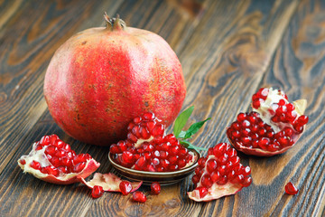 Juicy, ripe pomegranates, punica granatum fruit with leaves on wooden table close-up