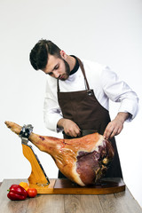 young cook in apron cuts appetizing ham 