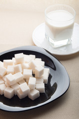 One glass of milk and sugar cubes on a black plate