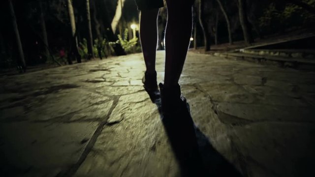 Suspicious hooded figure walks in a dark park at night