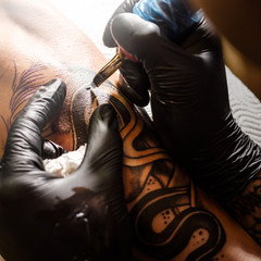Fototapeta na wymiar Hands of the artist tattooing on men's skin