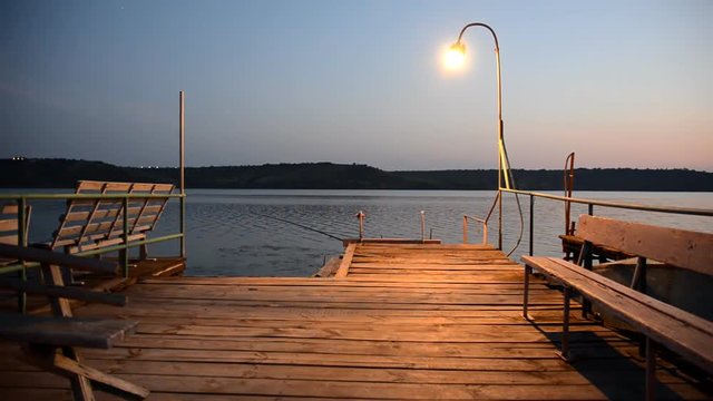 Wooden pier on the lake lit by lamp in the evening.