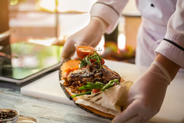 Cooked meat with vegetables. Thin pita bread on board. Grilled pork and thyme. Chef demonstrates new dish.