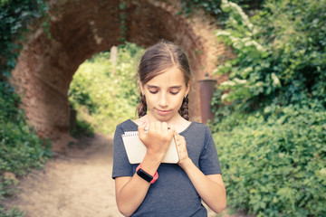 Small girl drawing in notebook near arch bridge
