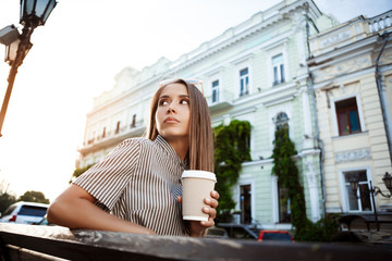 Fototapeta na wymiar Young beautiful girl sitting on bench, holding coffee. Outdoor background.